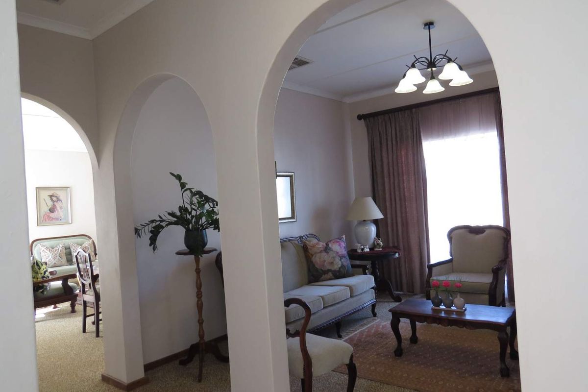 A view through arched doorways into a traditional living area featuring carpeted flooring and a central chandelier.