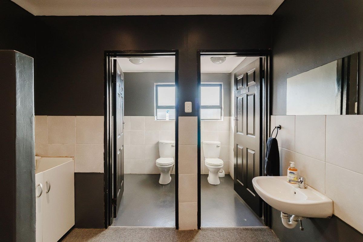 A functional commercial bathroom facility featuring two separate toilet cubicles and a wall-mounted basin with tiled splashback.