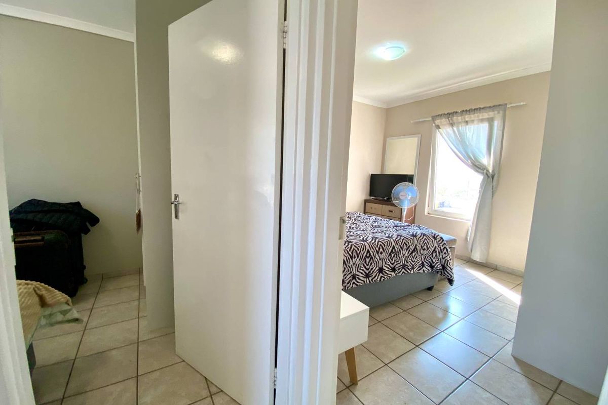 A bedroom view from the hallway, featuring tiled flooring and natural light through a window.