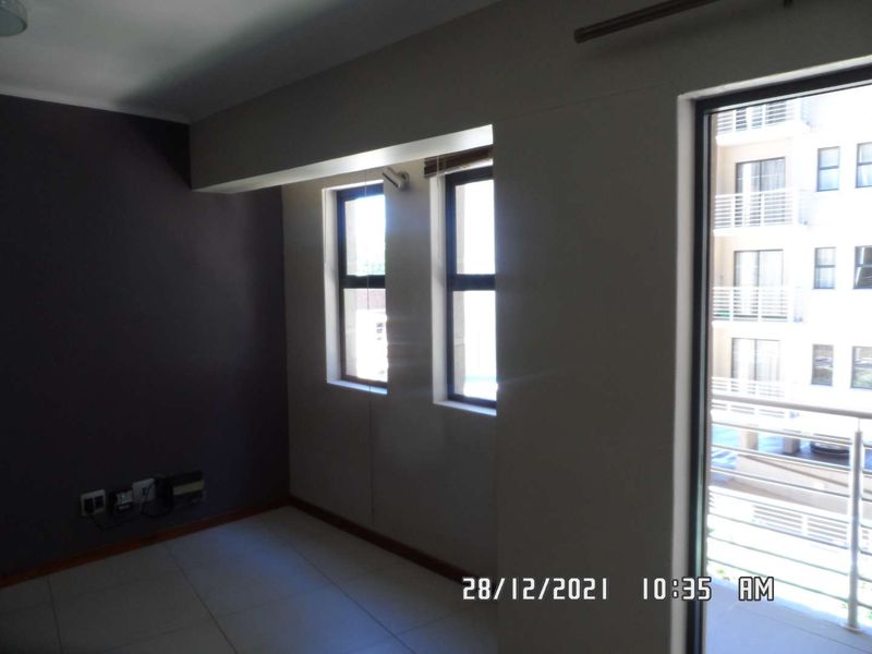 An empty living area featuring tiled flooring, large windows, and a sliding glass door leading to a balcony.