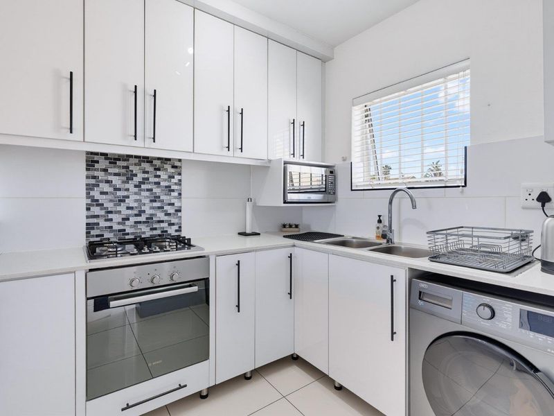 Modern kitchen featuring white cabinetry, stone countertops, tiled splashback, gas hob, electric oven, built-in microwave, and integrated laundry appliance space.