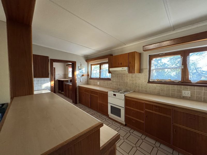 A functional kitchen featuring traditional wooden cabinetry, laminate countertops, a freestanding stove, and tiled finishes, offering potential for modern updates.