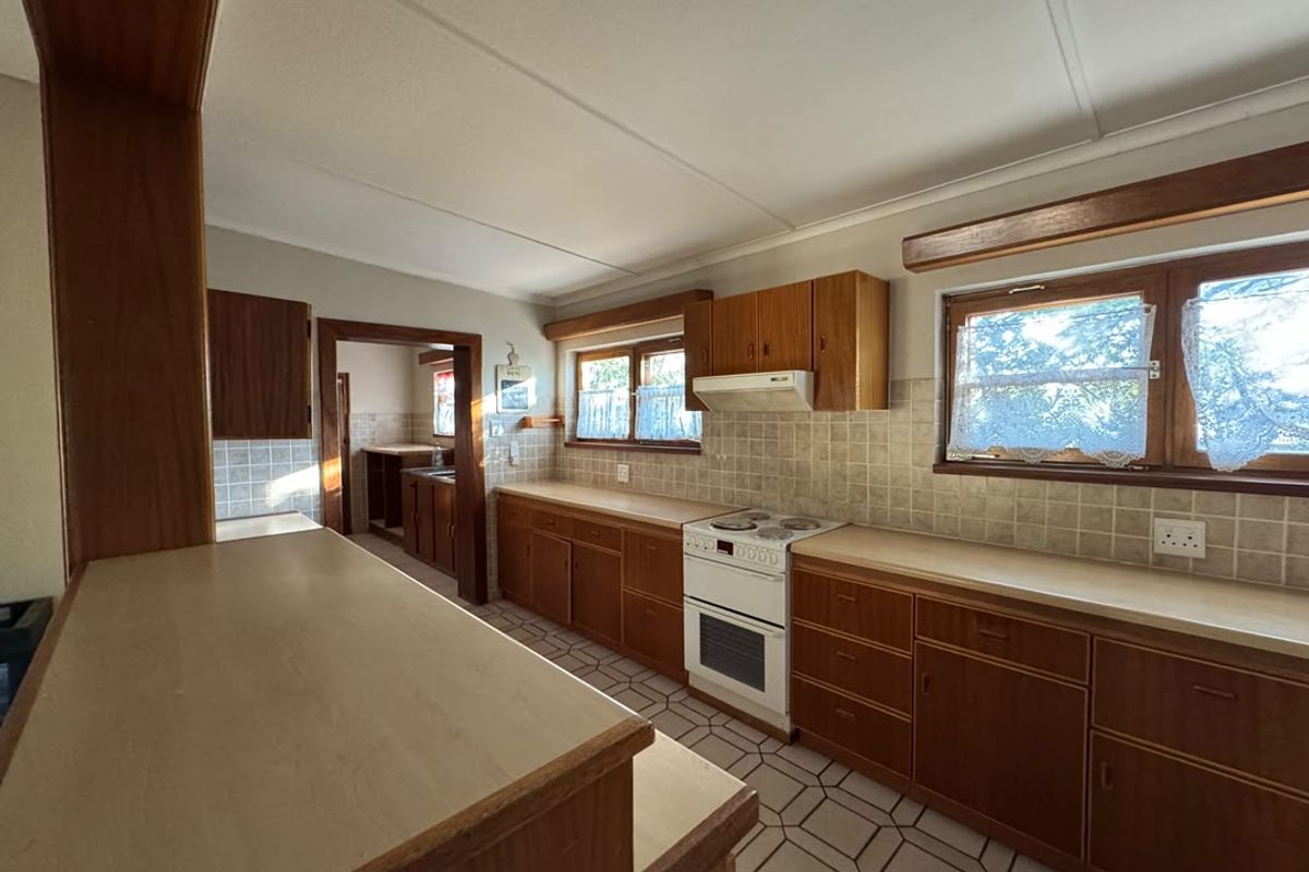 A functional kitchen featuring traditional wooden cabinetry, laminate countertops, a freestanding stove, and tiled finishes, offering potential for modern updates.