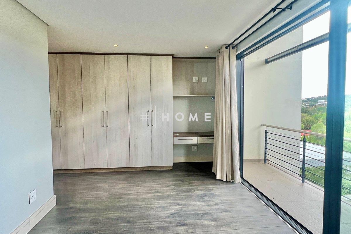 A bright bedroom featuring built-in cabinetry, a integrated desk area, wood-look flooring, and large sliding glass doors opening onto a private balcony.