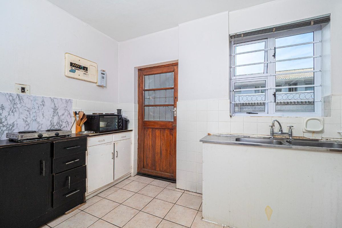 A functional kitchen featuring tiled flooring, a stainless steel sink, and built-in cabinetry, offering potential for modernization and cosmetic updates.