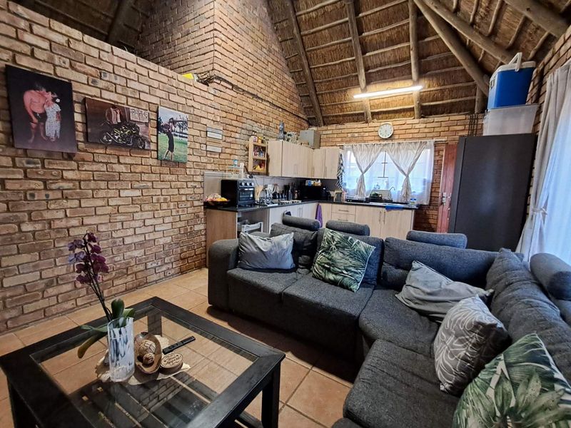 Open-plan living and kitchen area featuring rustic exposed brick walls, high vaulted thatched ceiling with timber rafters, and tiled flooring.