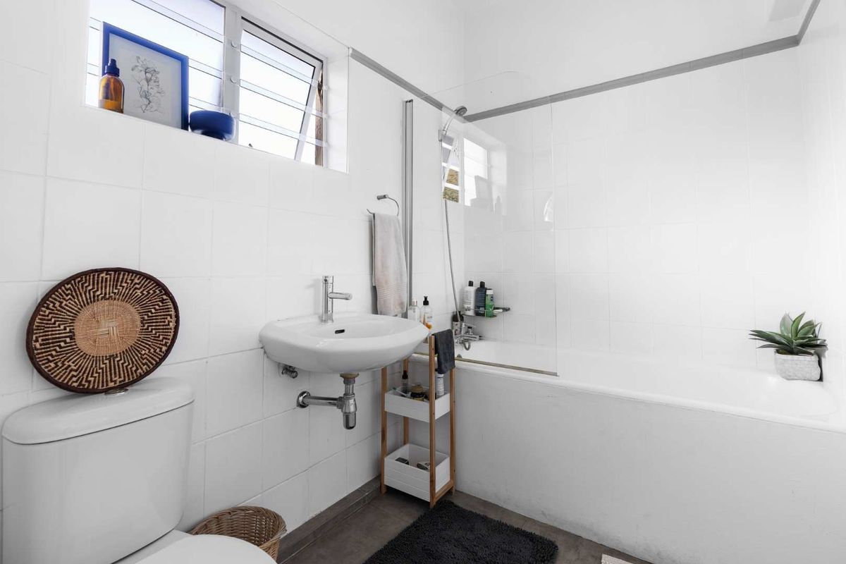 A functional bathroom featuring a wall-mounted basin, a bathtub with a glass shower screen, and louver windows for ventilation.