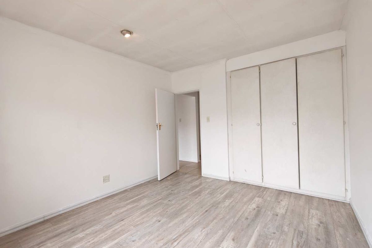 A bright, empty bedroom featuring light-toned laminate flooring and built-in storage cupboards, offering a clean canvas for personalization.
