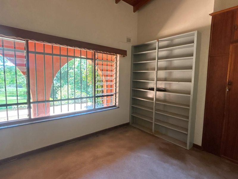 A vacant bedroom featuring built-in wooden cabinetry, metal shelving, and large windows with security bars, offering a blank canvas for renovation.