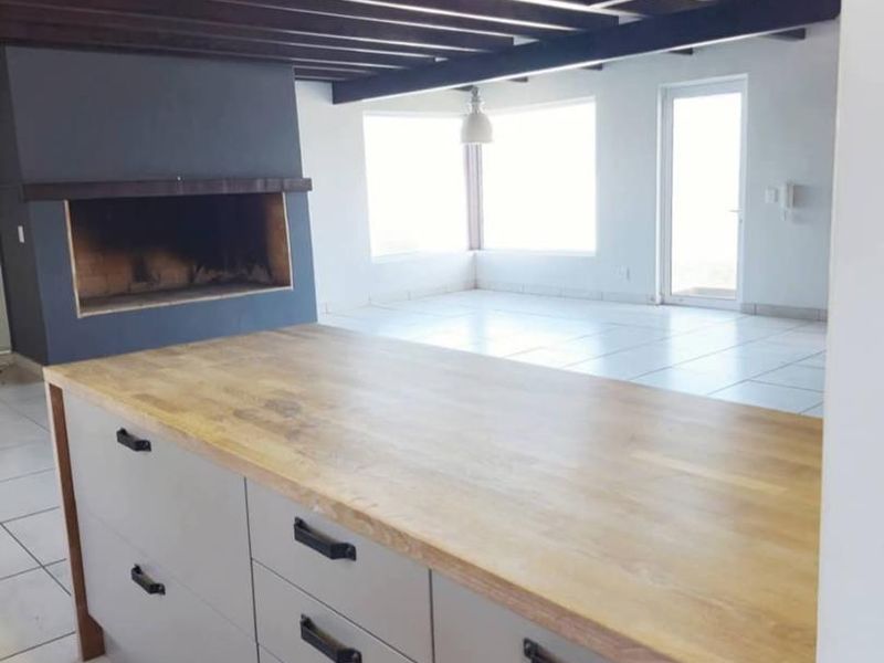 Spacious open-plan living area featuring a modern kitchen island with wooden countertop, exposed timber ceiling beams, and a built-in fireplace.