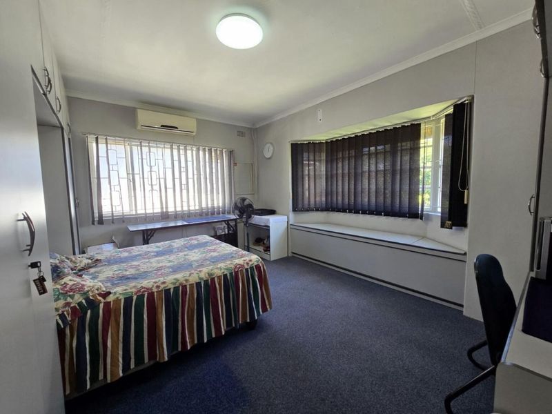 Spacious bedroom featuring built-in cupboards, a bay window with a built-in seat, and an air conditioning unit.