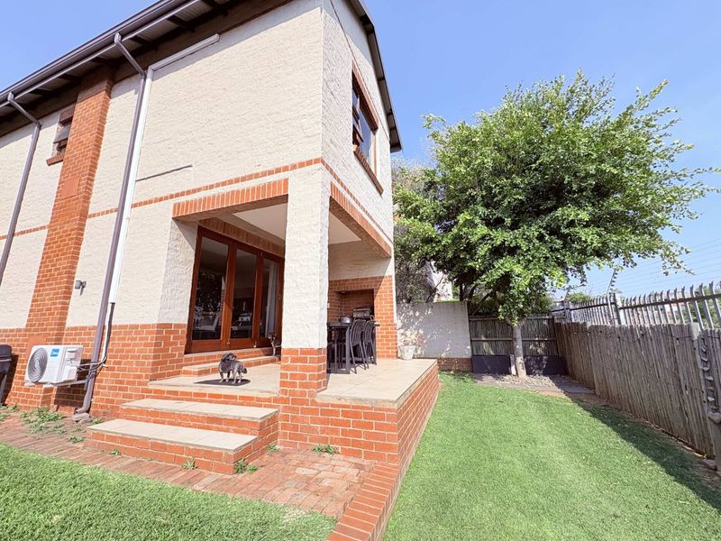 Rear view of the townhouse featuring a covered patio with a built-in braai, brick facade, and a private garden area.