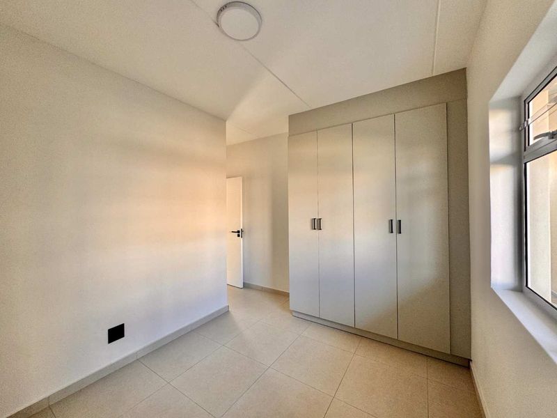 A clean, empty bedroom featuring neutral tiled flooring and modern built-in cupboards, offering a bright and versatile space ready for personalization.