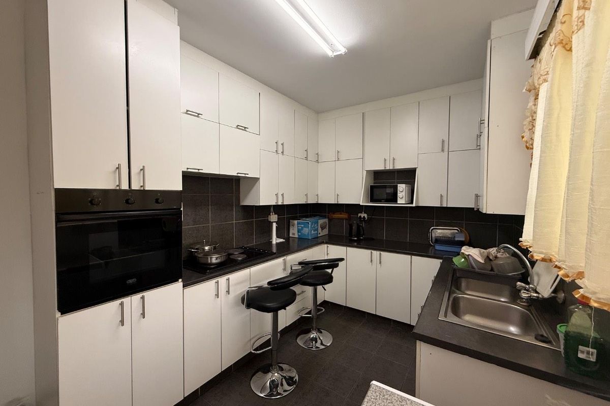 A functional kitchen featuring white cabinetry, dark countertops, a built-in oven, and a double-basin stainless steel sink with tiled backsplash.