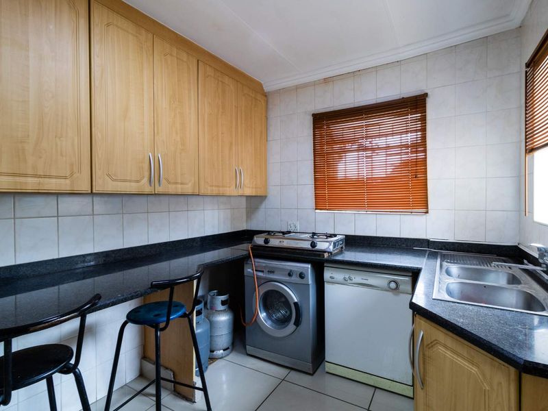 Functional kitchen featuring granite countertops, wooden cabinetry, tiled backsplash, and integrated sink, offering a practical layout for daily meal preparation.