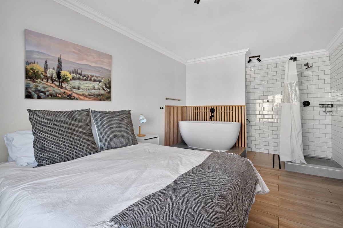 A modern bedroom featuring an open-plan ensuite with a freestanding bathtub and a walk-in shower with subway tile finishes.