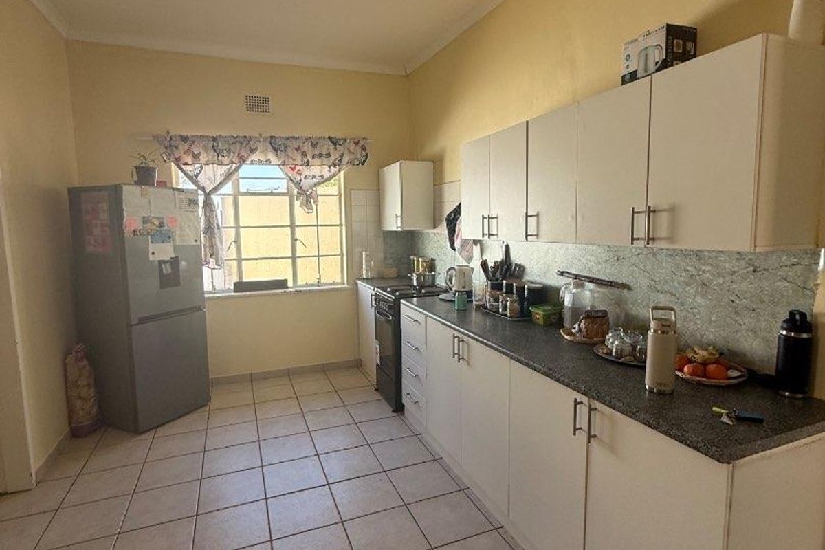 A functional kitchen featuring white cabinetry, laminate countertops, tiled flooring, and a window, offering a practical layout with potential for cosmetic updates.