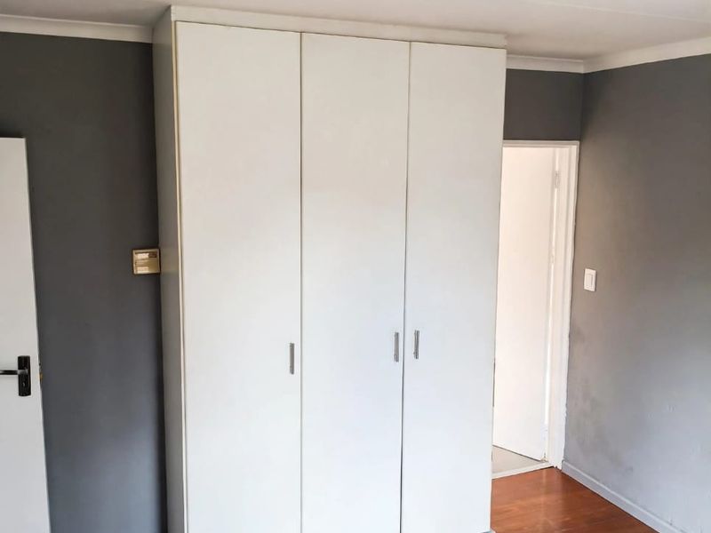 A clean, empty bedroom featuring laminate flooring and a large white built-in wardrobe with three doors.