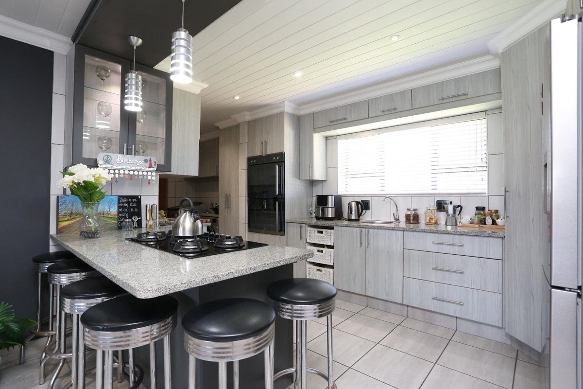 Modern kitchen featuring granite countertops, built-in oven, gas hob, and ample cabinetry with a breakfast bar and stylish pendant lighting.
