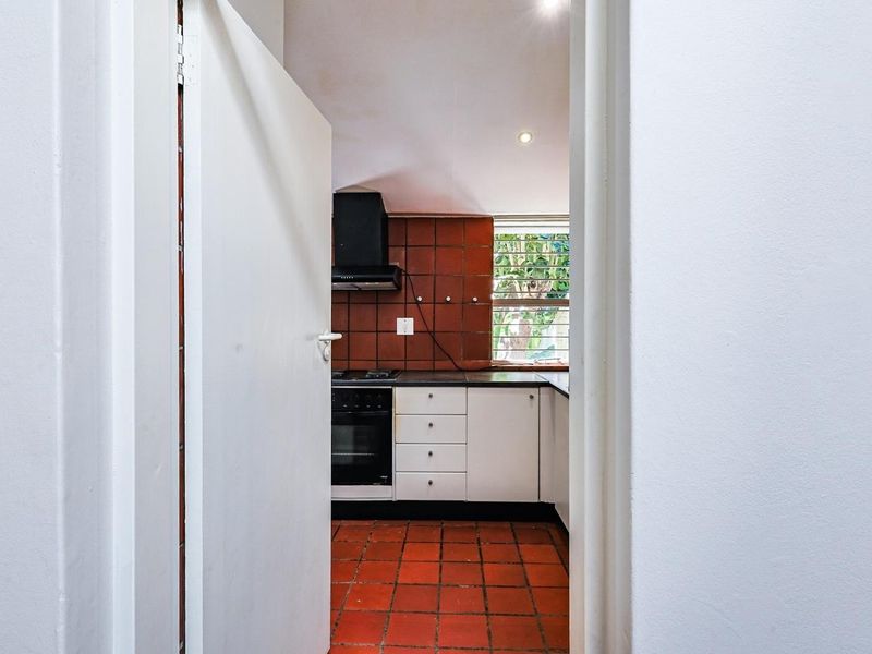 A functional kitchen featuring built-in cabinetry, a hob, oven, extractor fan, and traditional terracotta-style tiled flooring and backsplash.