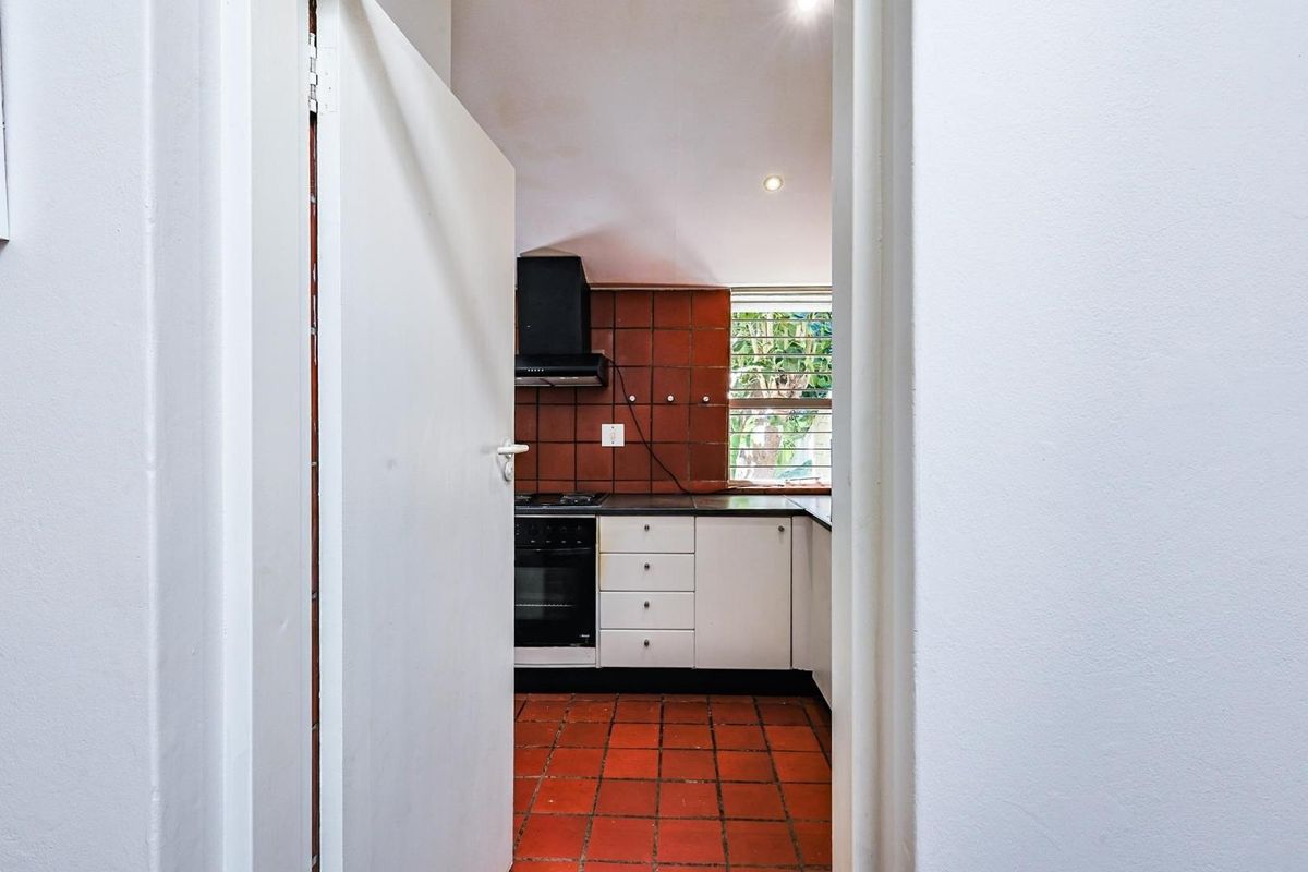 A functional kitchen featuring built-in cabinetry, a hob, oven, extractor fan, and traditional terracotta-style tiled flooring and backsplash.
