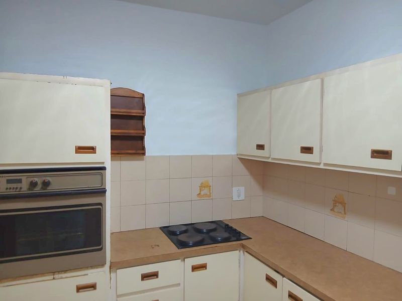 A dated kitchen featuring built-in cabinetry, a wall-mounted oven, and an electric hob with tiled backsplash.