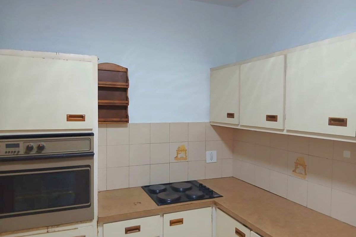 A dated kitchen featuring built-in cabinetry, a wall-mounted oven, and an electric hob with tiled backsplash.