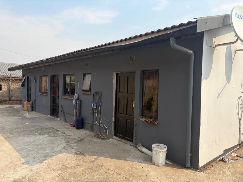 Rear exterior view of the property featuring a concrete driveway, security gates, and basic exterior finishes requiring maintenance.
