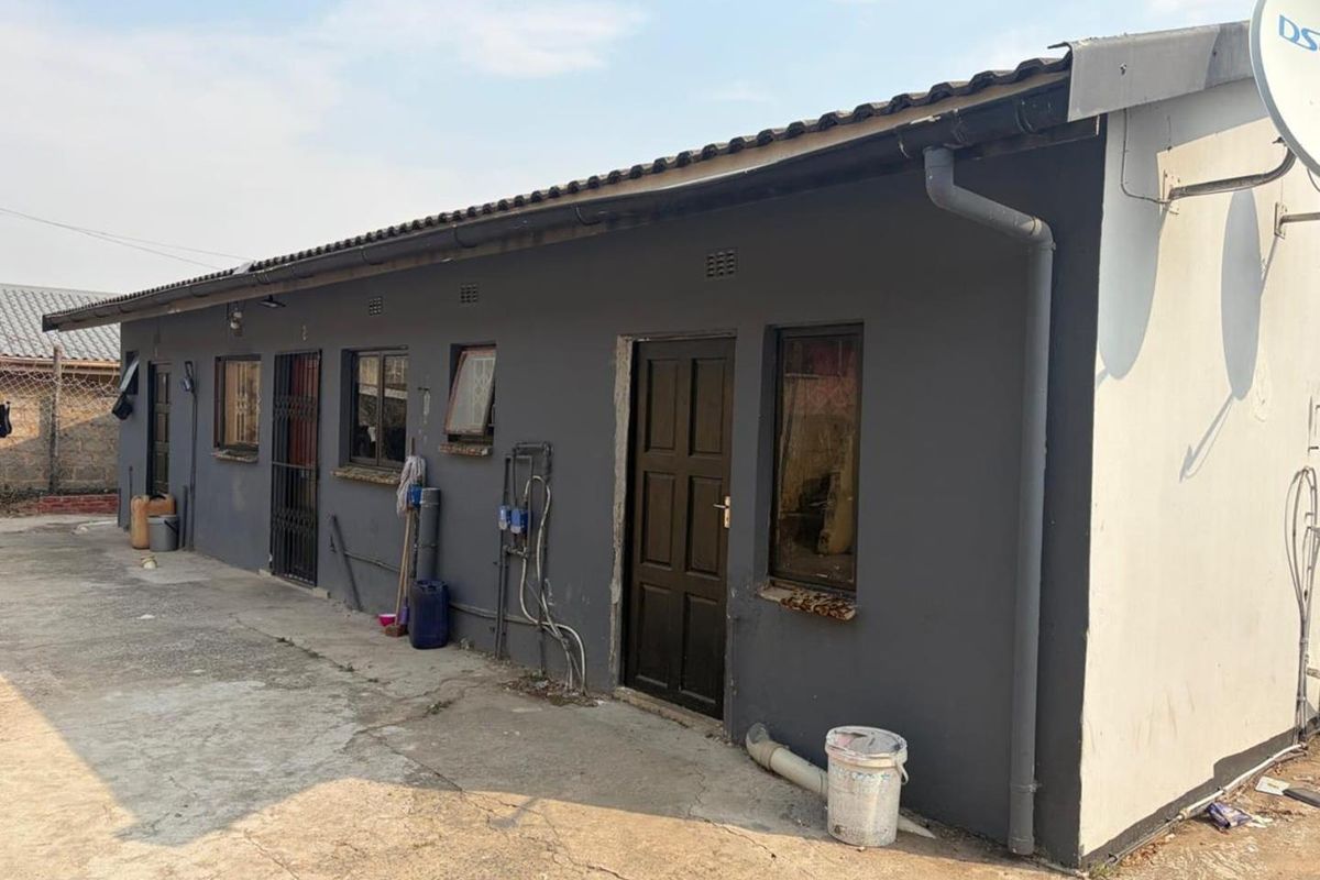 Rear exterior view of the property featuring a concrete driveway, security gates, and basic exterior finishes requiring maintenance.