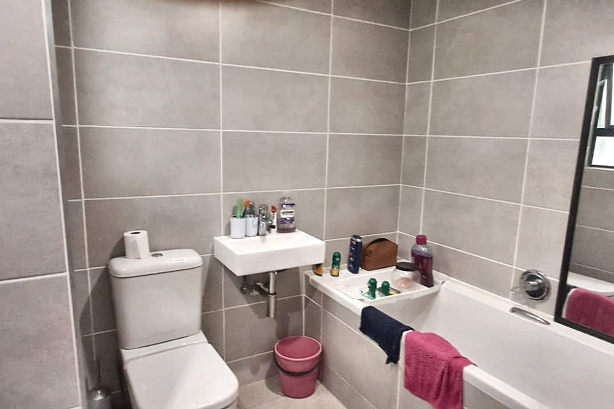A modern bathroom featuring grey wall tiles, a wall-mounted basin, a standard toilet, and a bathtub with a wall-mounted mirror.