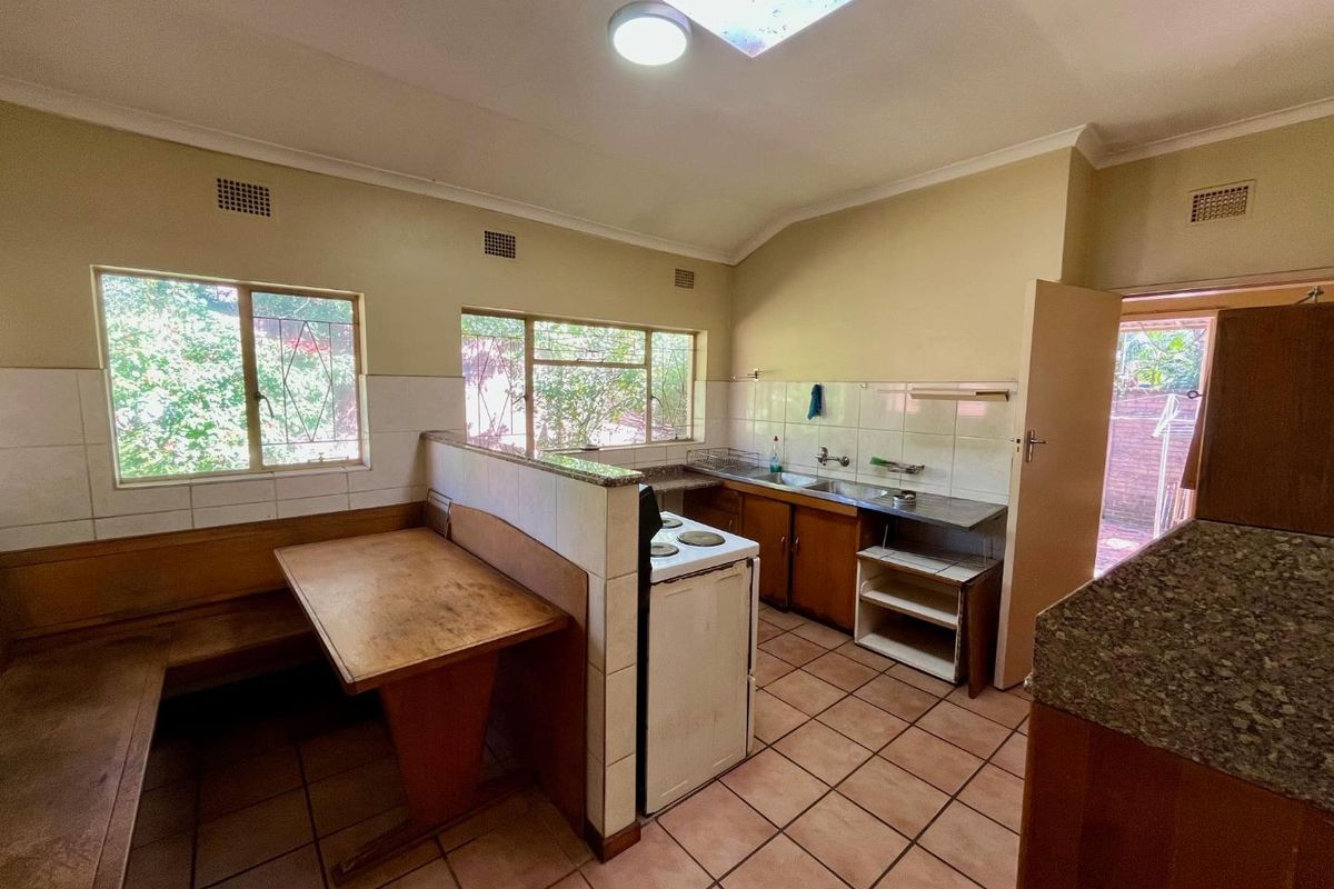 A dated kitchen featuring built-in cabinetry, a freestanding stove, tiled flooring, and a built-in breakfast nook area with natural light.