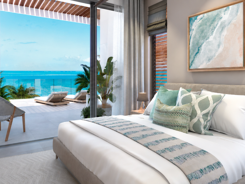 Modern bedroom featuring floor-to-ceiling sliding glass doors that open onto a private balcony with stunning ocean views and a glass balustrade.