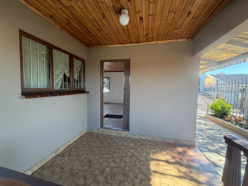 A covered outdoor patio area featuring a timber ceiling, tiled flooring, and security bars on the windows, providing a functional transition space.