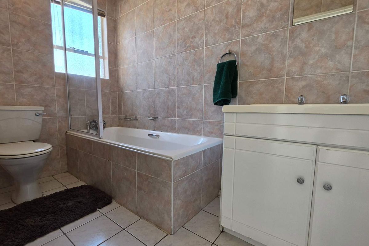 A functional bathroom featuring a built-in vanity, bathtub with a glass shower screen, and full-height wall tiling.