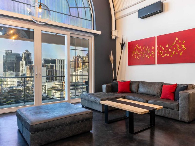 Modern living room featuring high vaulted ceilings, polished concrete floors, and large arched windows with expansive city views and balcony access.