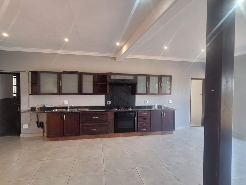 Spacious open-plan kitchen featuring dark wood cabinetry, granite countertops, integrated appliances, and tiled flooring, offering a functional and well-lit cooking area.
