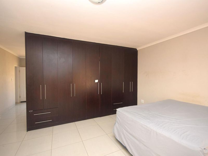 A bedroom featuring extensive dark wood built-in cupboards and neutral tiled flooring.