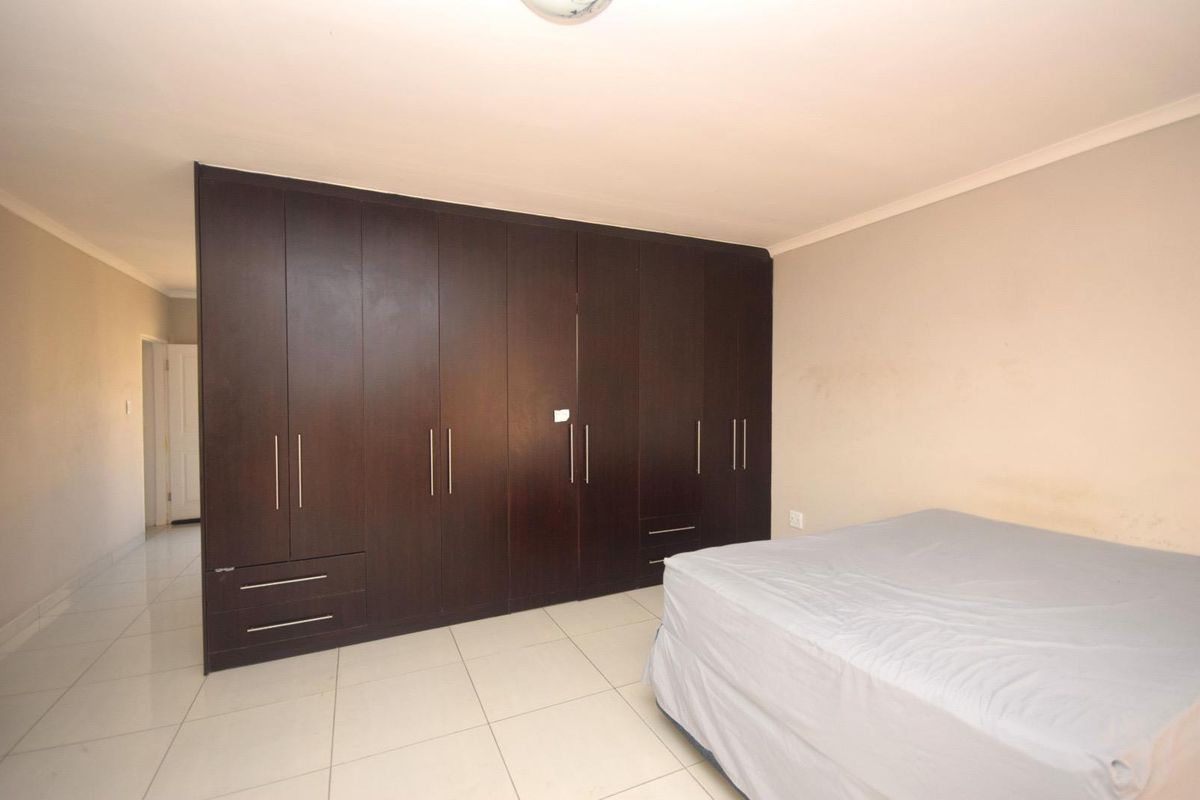 A bedroom featuring extensive dark wood built-in cupboards and neutral tiled flooring.