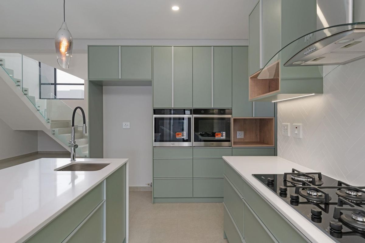 Modern kitchen featuring sage green cabinetry, stone countertops, integrated double ovens, gas hob, and a central island with a sink.