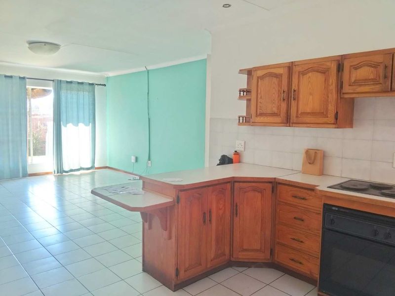 Open-plan living and kitchen area featuring dated wooden cabinetry, tiled flooring, and direct access to an outdoor space through sliding glass doors.
