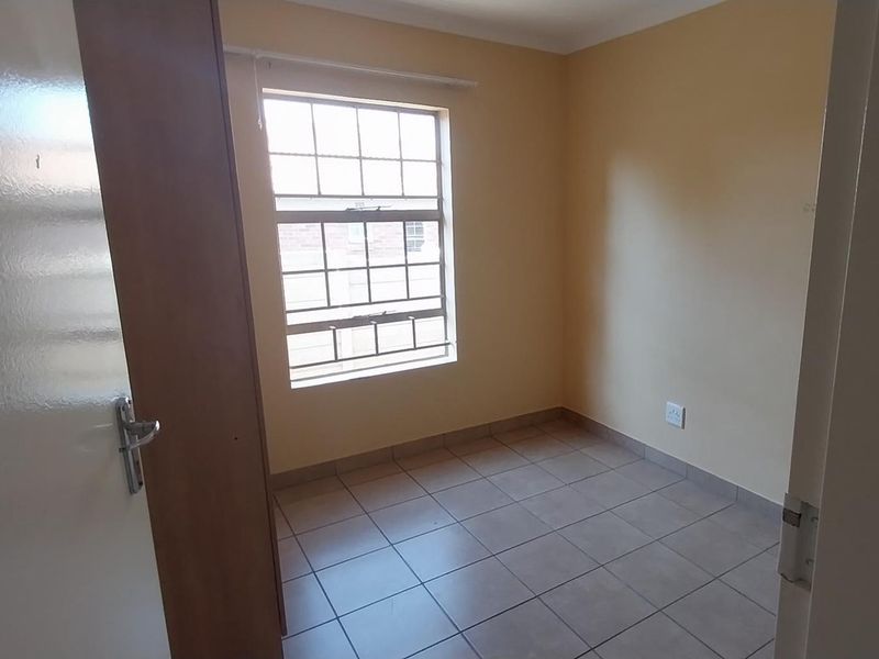 A vacant bedroom featuring tiled flooring and a window with security bars, offering a clean, neutral space ready for personalization.