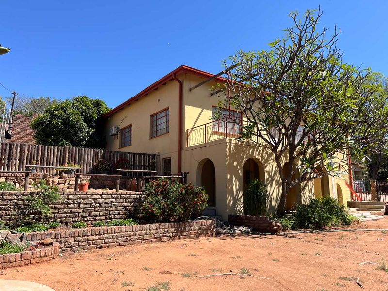 Rear view of the property featuring a stone retaining wall, a raised balcony with metal railing, and an arched patio area.