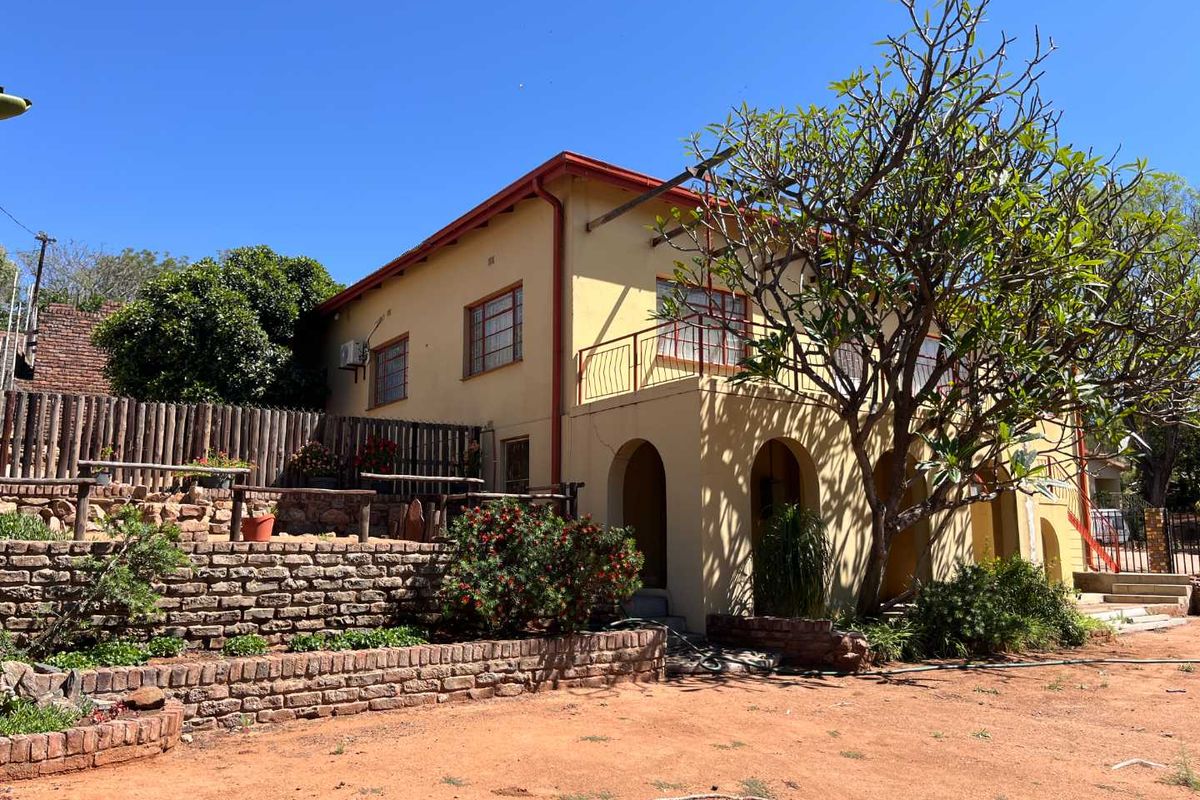 Rear view of the property featuring a stone retaining wall, a raised balcony with metal railing, and an arched patio area.