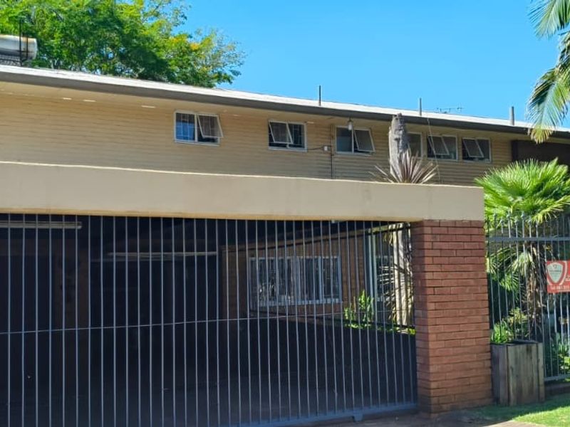 Front exterior view of the property featuring a brick boundary wall, metal security gate, and solar water heating system on the roof.
