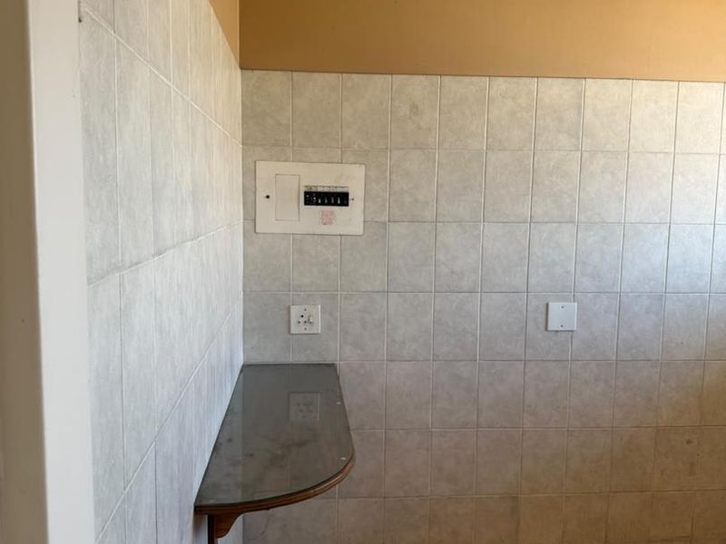 A functional utility space featuring tiled walls and flooring, a wall-mounted shelf, and an integrated electrical distribution board.