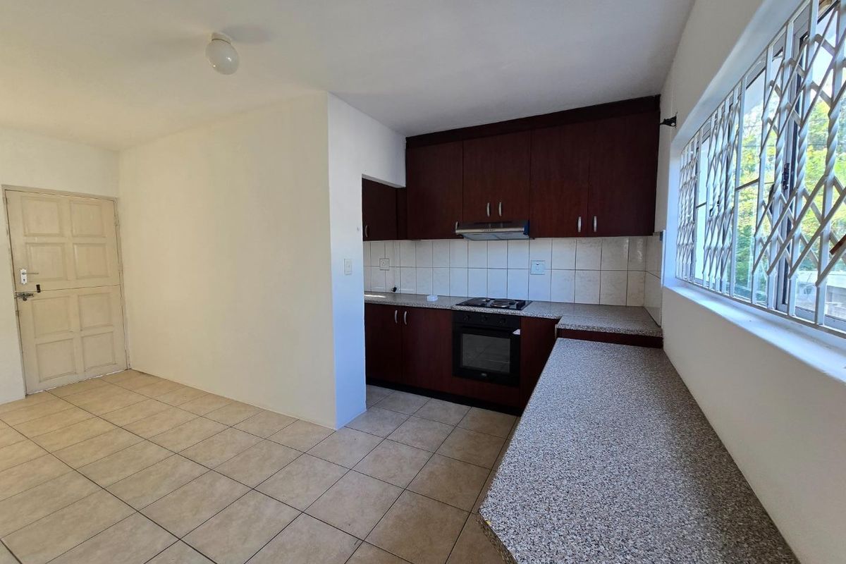 A functional kitchen featuring dark wood cabinetry, laminate countertops, built-in oven with gas hob, and tiled flooring, offering a clean and practical workspace.