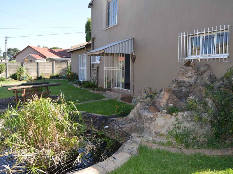 Rear garden area featuring a lawn, a rockery water feature with a pond, and a building exterior with security bars and a metal awning.