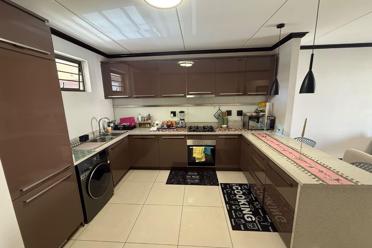 Modern kitchen featuring high-gloss cabinetry, stone countertops, integrated appliances, and a breakfast bar with pendant lighting.