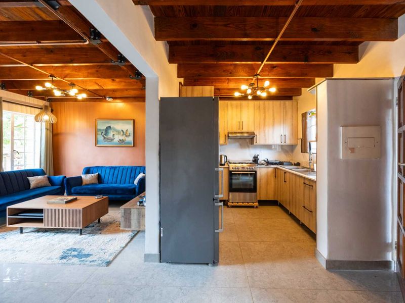 Open-plan living and kitchen area featuring exposed timber ceiling beams, light wood cabinetry, and modern tiled flooring throughout.