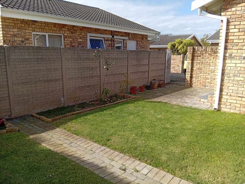 A private rear garden area featuring a well-maintained lawn, brick paved pathways, and secure precast concrete boundary walls.